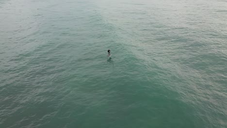 Aerial-view-following-a-man-on-an-electric-hydrofoil-personal-water-craft-surfboard-riding-in-the-ocean-at-sunrise,-the-future-of-electric-water-transportation-and-vehicles