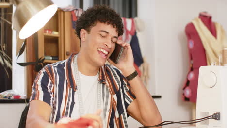 diseñador de moda masculino biracial dibujando diseño y hablando en teléfono inteligente en estudio, cámara lenta