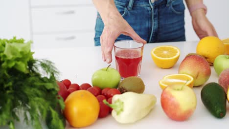 woman hand takes a glass of fresh juice from the kitchen table with fruits