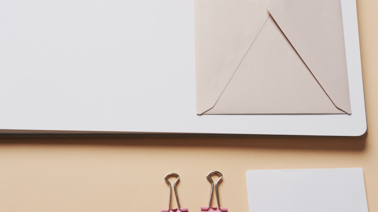 슬로우 모션으로 베이지색 배경에 배열된 노트북, 펜 및 서류의 클로즈업