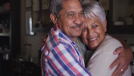 Feliz-Pareja-De-Raza-Mixta-Senior-Sonriendo-Y-Abrazándose-En-La-Cocina