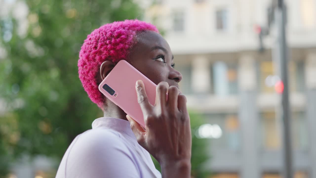 Woman with pink hair talking on a phone call outdoors in the city