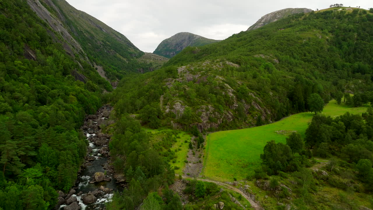 Forward aerial reveals a river valley, green pastures and forested slopes in southwest Norway