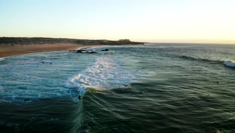 sunset drone shot of surfers catching waves on praia do guincho on cascais - sintra