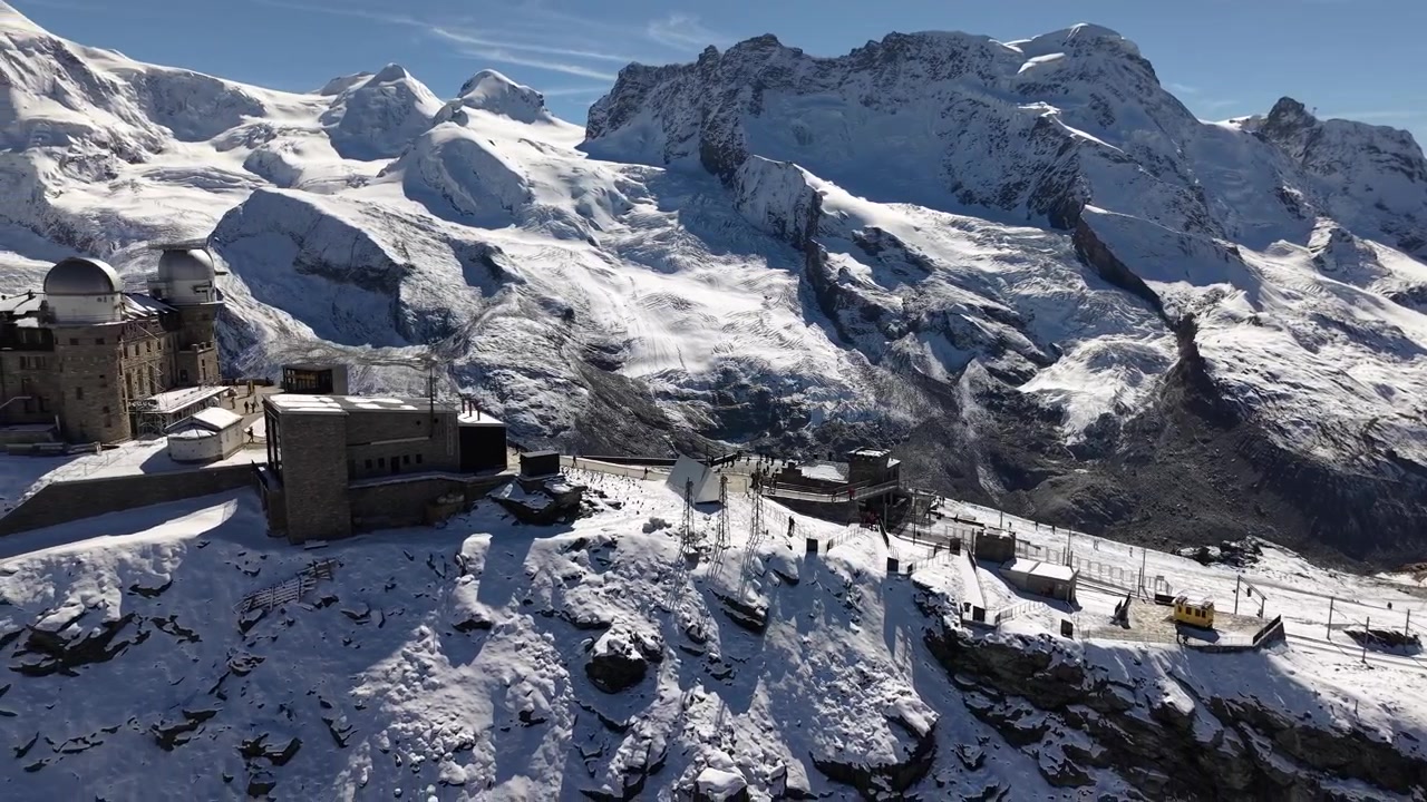 Sorvolo aereo vicino all'osservatorio del Gornergrat a Zermatt, Svizzera, con vista sulla stazione ferroviaria e sulle cime del Monte Dufourspitze in una giornata autunnale nevosa nelle Alpi svizzere.