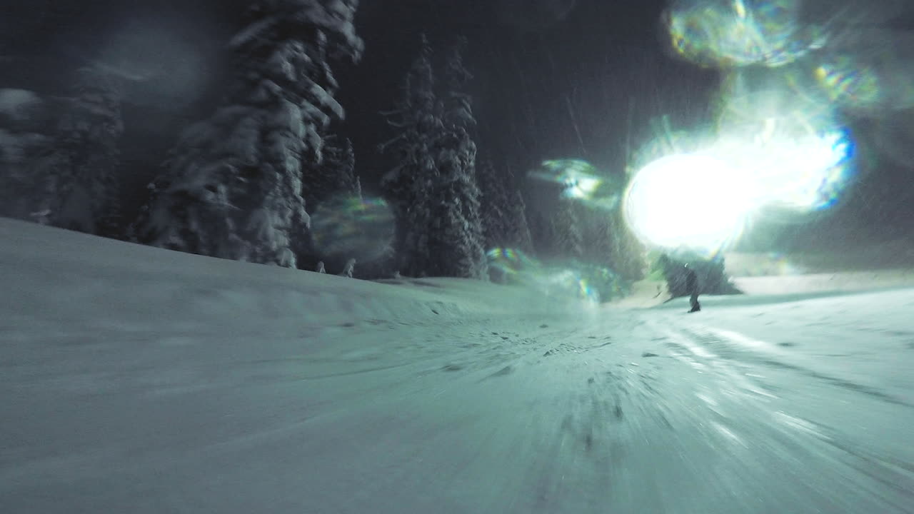 Snowboarding night session. Two people ride together down a mountain at night. There is glow and shine as the lights reflect on the snow.