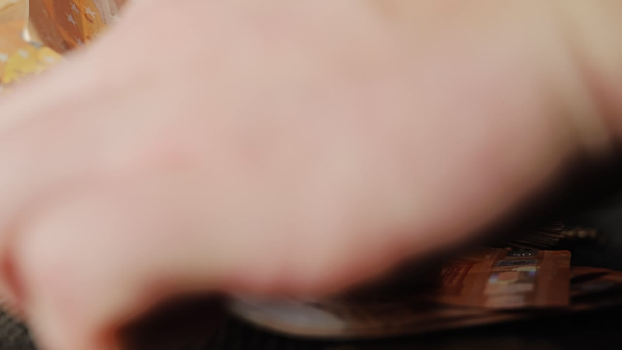 Una mano prende banconote in euro come proiettili e monete bitcoin rimangono su un pavimento scuro.