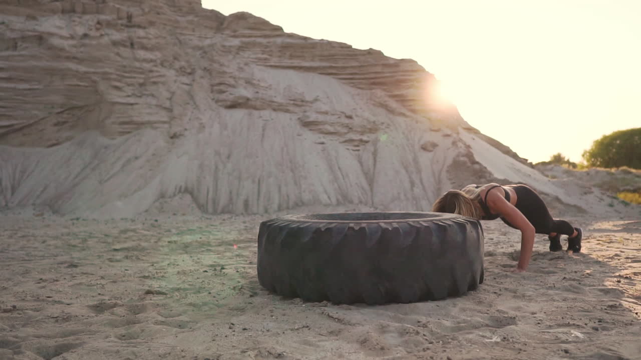 chica en una cantera de arena saltando burpee con flexiones a través de la rueda en la arena