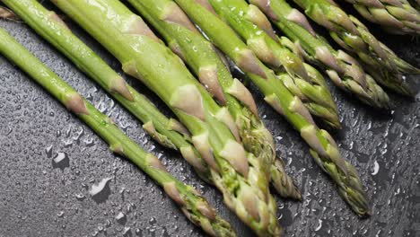 raw green asparagus on wet black slate background. rotating