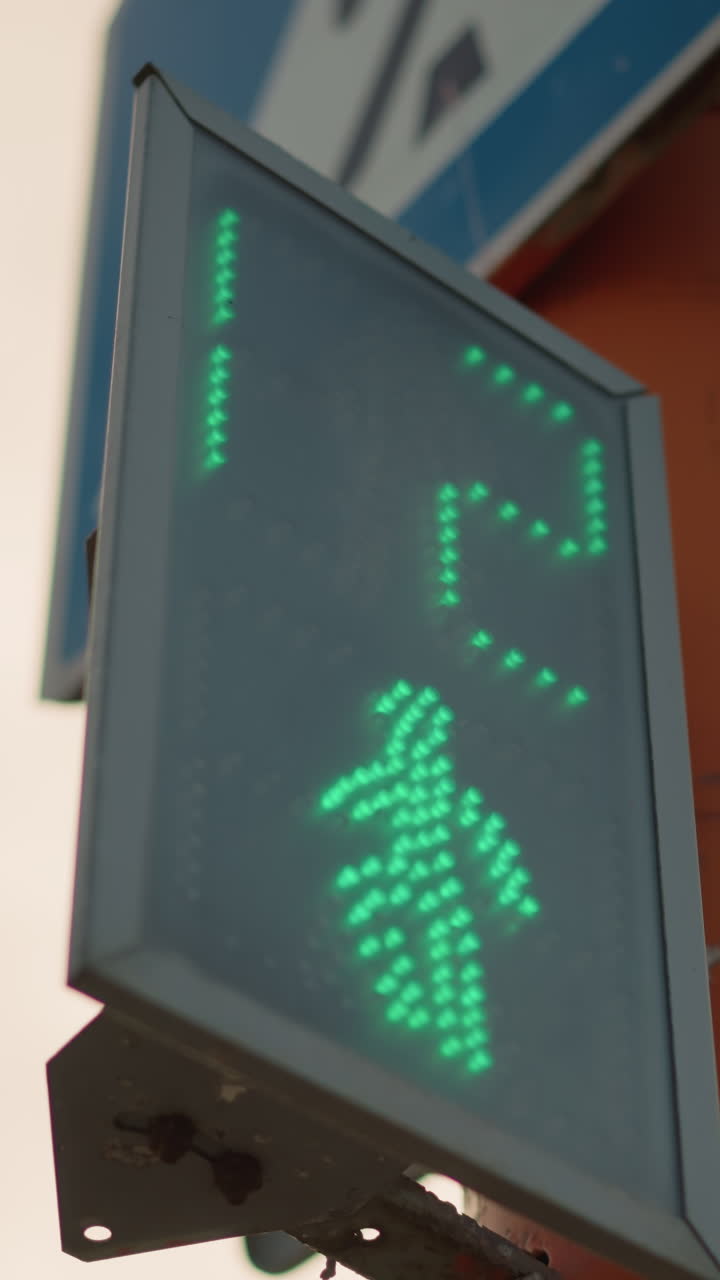 green LED pedestrian signal with countdown display, angled street mount showing dot matrix pixels and numeric timer, conveys active crossing permission and urban intersection timing for commuters