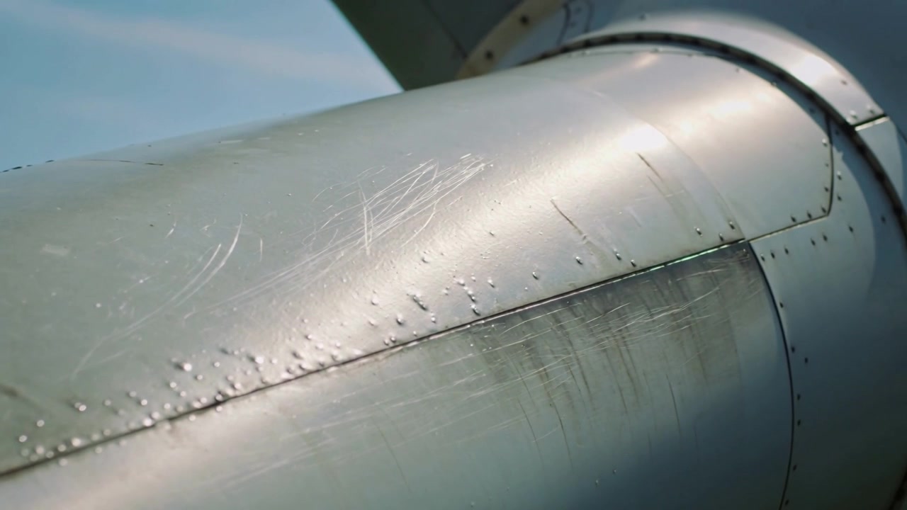 Panoramica di una navicella di aereo nel cielo aperto, la telecamera mostra rivetti, graffi e un giunto rotondo per il controllo.