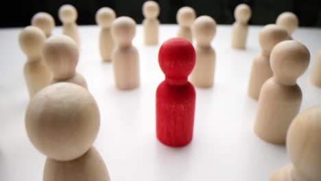 one red figure standing out in a crowd of wooden people