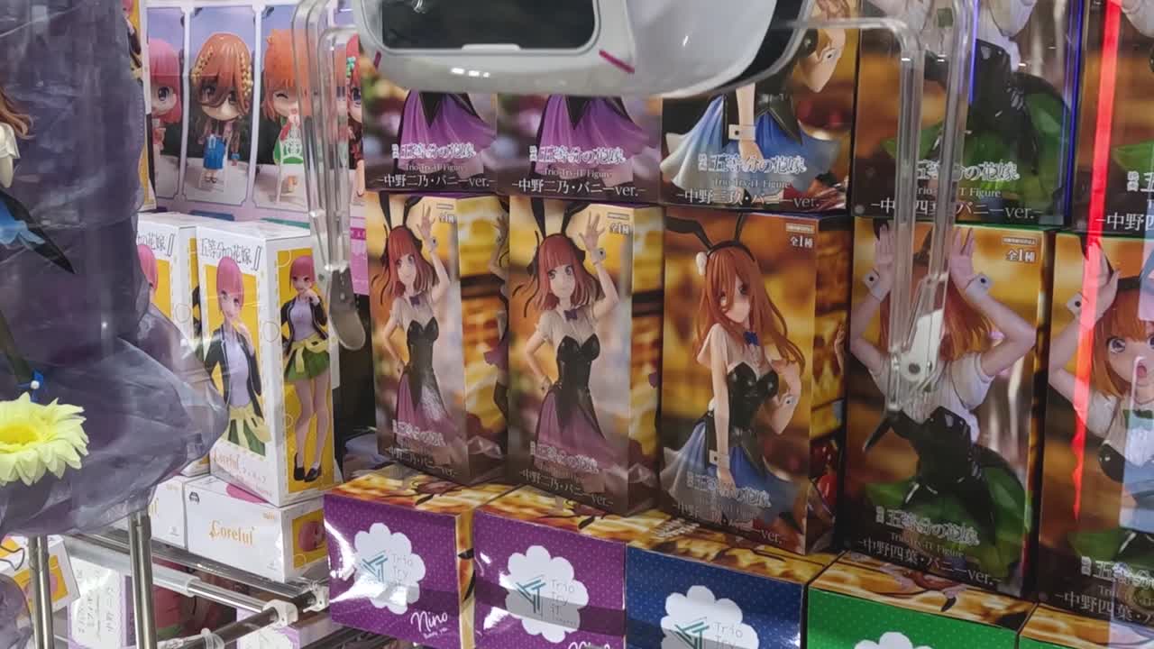 A claw machine attempts to grab an anime figure box using precise controls and timing.