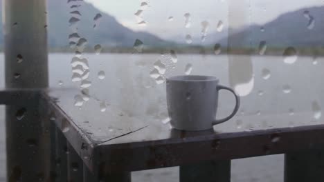 Animación-De-Gotas-De-Lluvia-Sobre-La-Ventana,-Una-Taza-De-Café,-Un-Lago-Y-Un-Paisaje