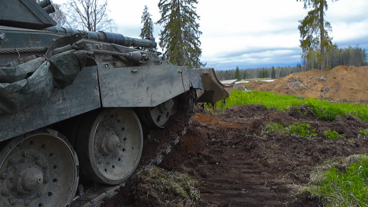 Rare and amazing close up or close up footage of a British Challenger 2 4034 bulldozer tank hidden in a muddy field or forest and taking aim in the distance with its large metal cannon artillery gun.