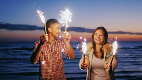 pareja joven divirtiéndose con fuegos artificiales en las manos los fuegos artificiales encendieron la pareja riendo pasando un buen ti