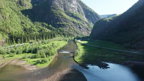 Approaching-the-river-of-Dale-in-beautiful-idyllic-landscape-Dalevagen-during-sunrise---Forward-moving-aerial-in-between-road-E16-and-bergensbanen-railway