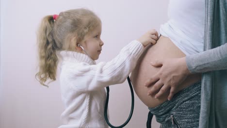 Lustiges-Mädchen-Legt-Stethoskop-Auf-Den-Bauch-Schwangerer-Mama-Im-Zimmer