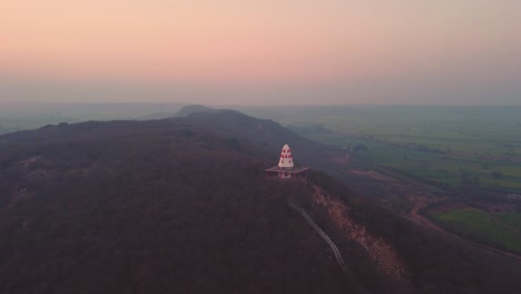 tomada aérea de un templo hindú en la cima de una colina con escaleras que llevan a él durante la hora de la puesta del sol en un pueblo de gwalior en madhya pradesh, india