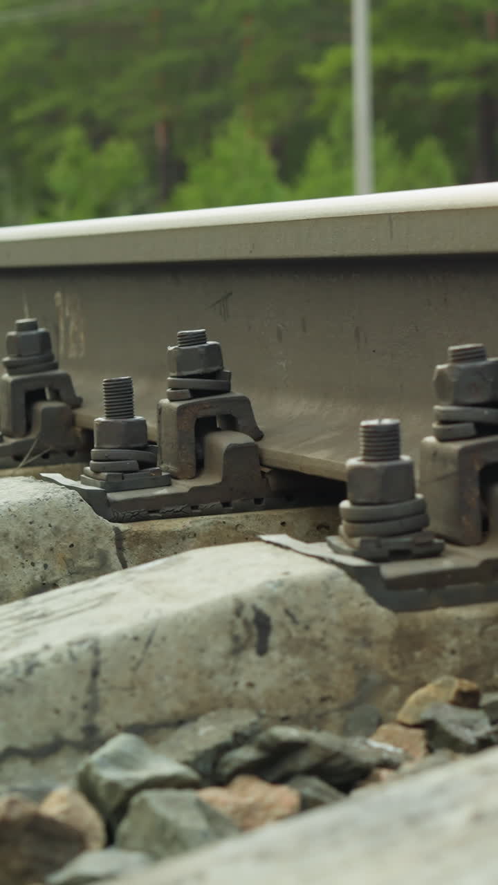 콘크리트 스프리터에 레일을 고정하는 볼트 및 나트와 함께 철도 트랙 고정 장치의 근접 시각, 배경에 자갈과 식물의 시각