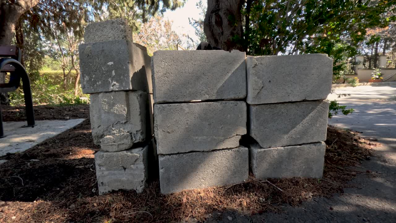 Concrete blocks are stacked next to a tree in a garden area on a sunny afternoon. The project shows a part of ongoing construction work. Surrounding plants and trees add to the setting