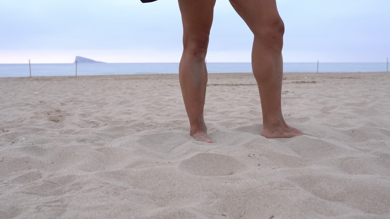 Crop strong athlete throwing dumbbell on sand on beach