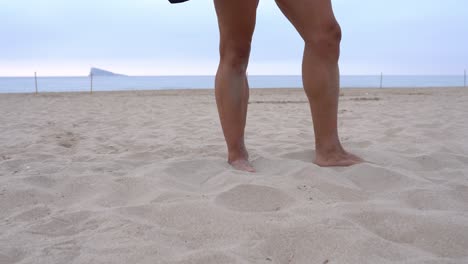 crop strong athlete throwing dumbbell on sand on beach