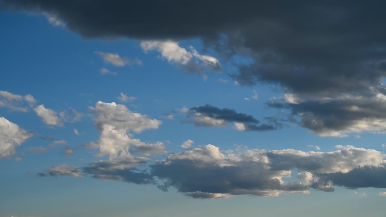 Time lapse of multiple layers of white and dark grey blowing clouds moving across a bright blue sky.