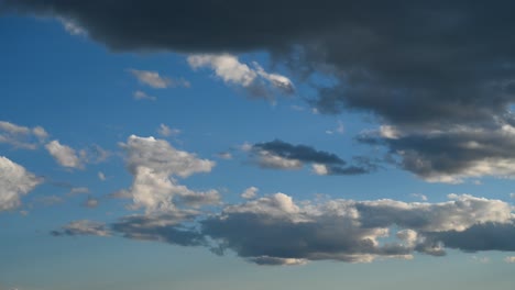 time lapse of multiple layers of white and dark grey blowing clouds moving across a bright blue sky.