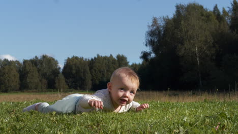 a baby crawling on green grass under a clear sky with trees in the background