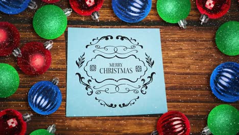 sneeuw vallen en vrolijk kerstfeest tekst nota en bauble decoraties op hout