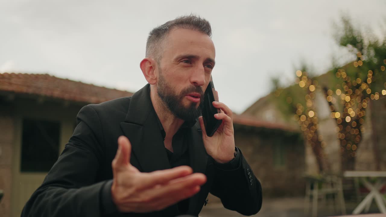angry man in black suit argues on phone with hand gesture outdoors
