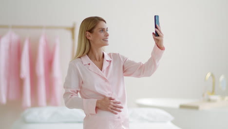 pregnant woman taking a selfie in pink pajamas