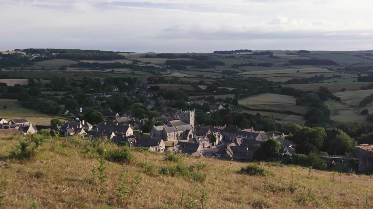 Panoramica statica di un villaggio rurale inglese visto da una collina sotto il sole.