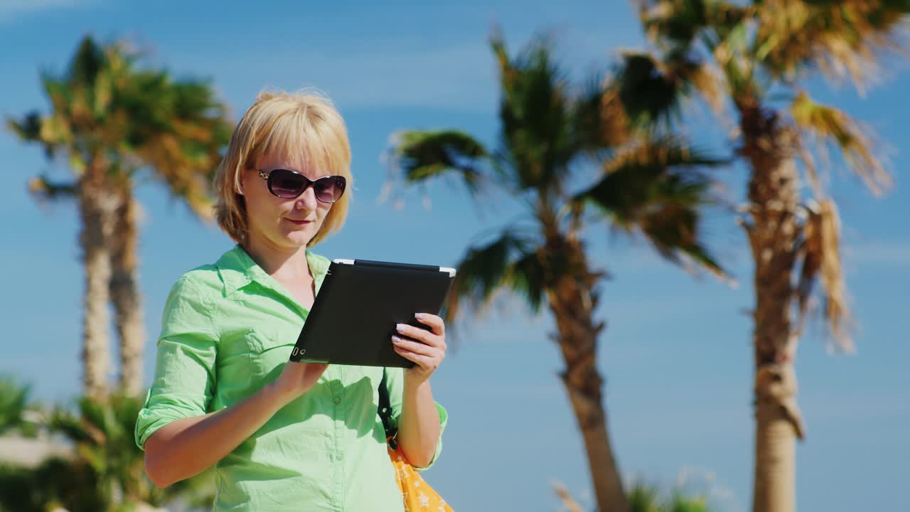 A Woman In A Light Green Shirt Using Tablet Against The Sky And Palm Trees