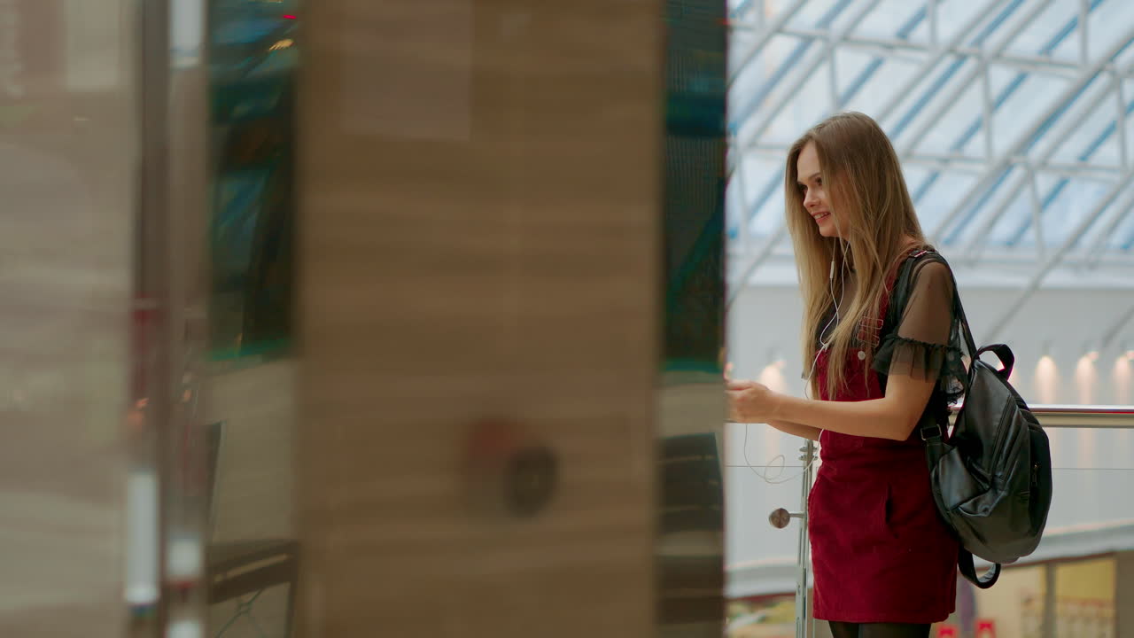 Portrait of cheerful teen girl enjoying music in stereo accessory connected to smartphone entertaining on coffee break, smiling woman listening radio broadcast via app on cellular sitting in cafe