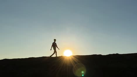 Young-silhouetted-man-walks-across-golden-hour-sunset
