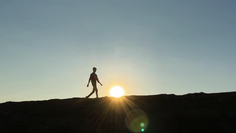 ein junger, silhouettierter mann geht über den sonnenuntergang zur goldenen stunde