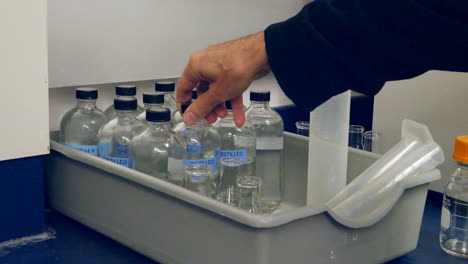 Primer-Plano-De-Un-Científico-Reemplazando-Un-Recipiente-De-Agua-Destilada-Para-Un-Experimento-En-Un-Laboratorio-De-Investigación-Médica