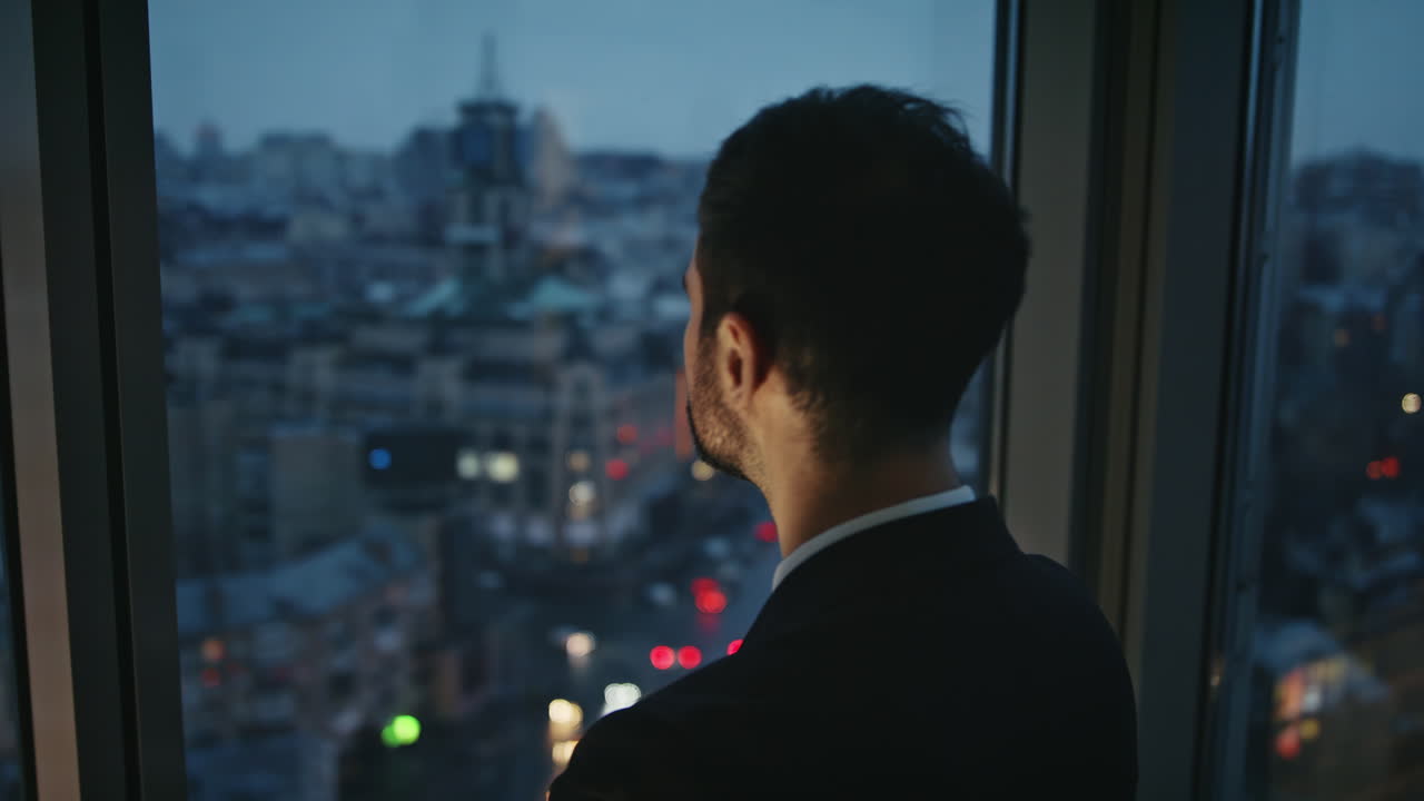hombre de negocios pensativo mirando el paisaje de la ciudad por la noche en la ventana de la oficina solo cerca