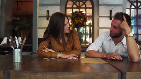 nice couple are sitting together in a restaurant. she is drinking some tea and looking to a menu while her biyfriend is trying to pick food for them. also he is giving food advices to her.