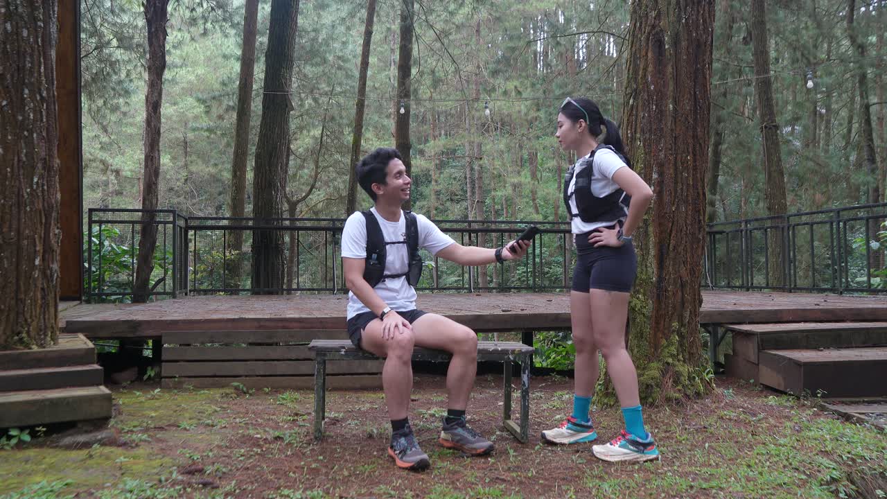 Asian couple taking photo with smartphone during outdoor trail run in Indonesian forest