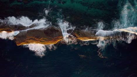 bathed in golden morning light, a lone rock sits surrounded by shimmering sea. gentle waves swirl around it, creating a calm and timeless coastal moment near warden head, ulladulla, nsw, australia.