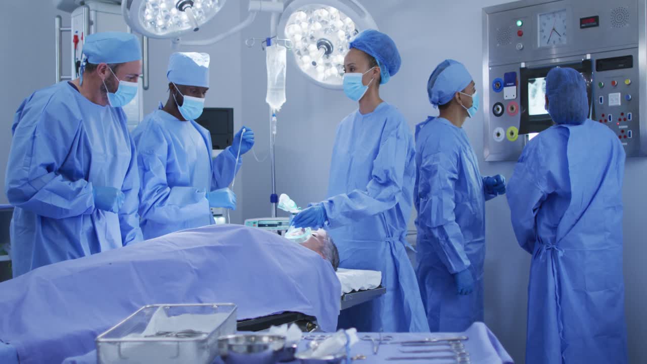 cirujanos de raza mixta con ropa de protección poniendo al paciente a dormir en el quirófano