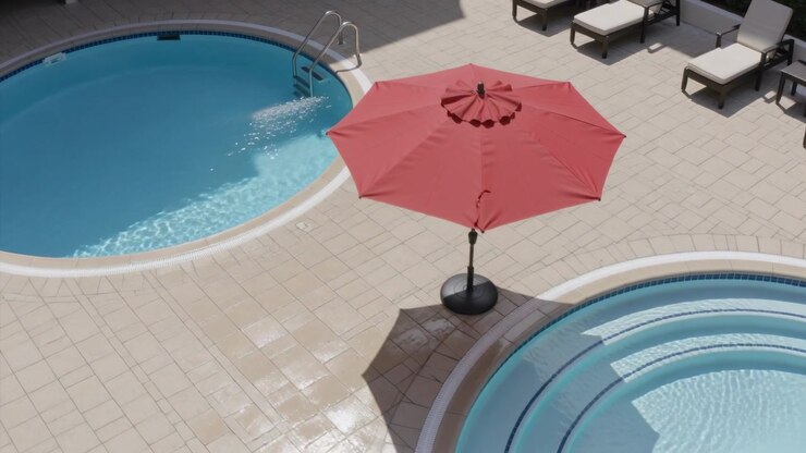 Panning aerial camera showing red patio umbrella over two round pools, revealing water jet rippling
