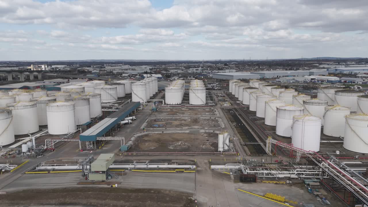 Aerial top-down of grid of massive cylindrical gas holders linked by pipelines and access roads, depicting large-scale energy storage infrastructure