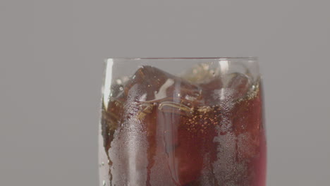 cubo de hielo cayendo en un vaso de cola con el líquido salpicando a cámara lenta