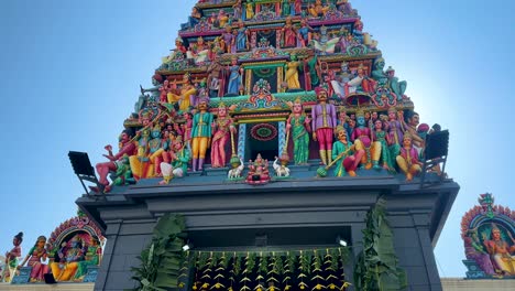 camera tilts upward revealing intricate, vibrant sculptures on a hindu temple gopuram under clear daylight, highlighting detailed architecture and festive atmosphere
