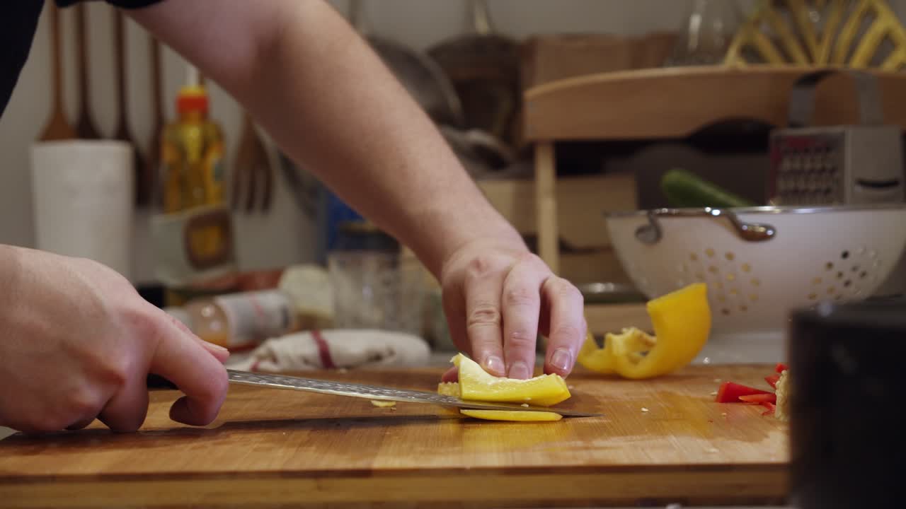 el chef corta pimienta de color amarillo grande con un cuchillo de acero en una tabla cortada de madera