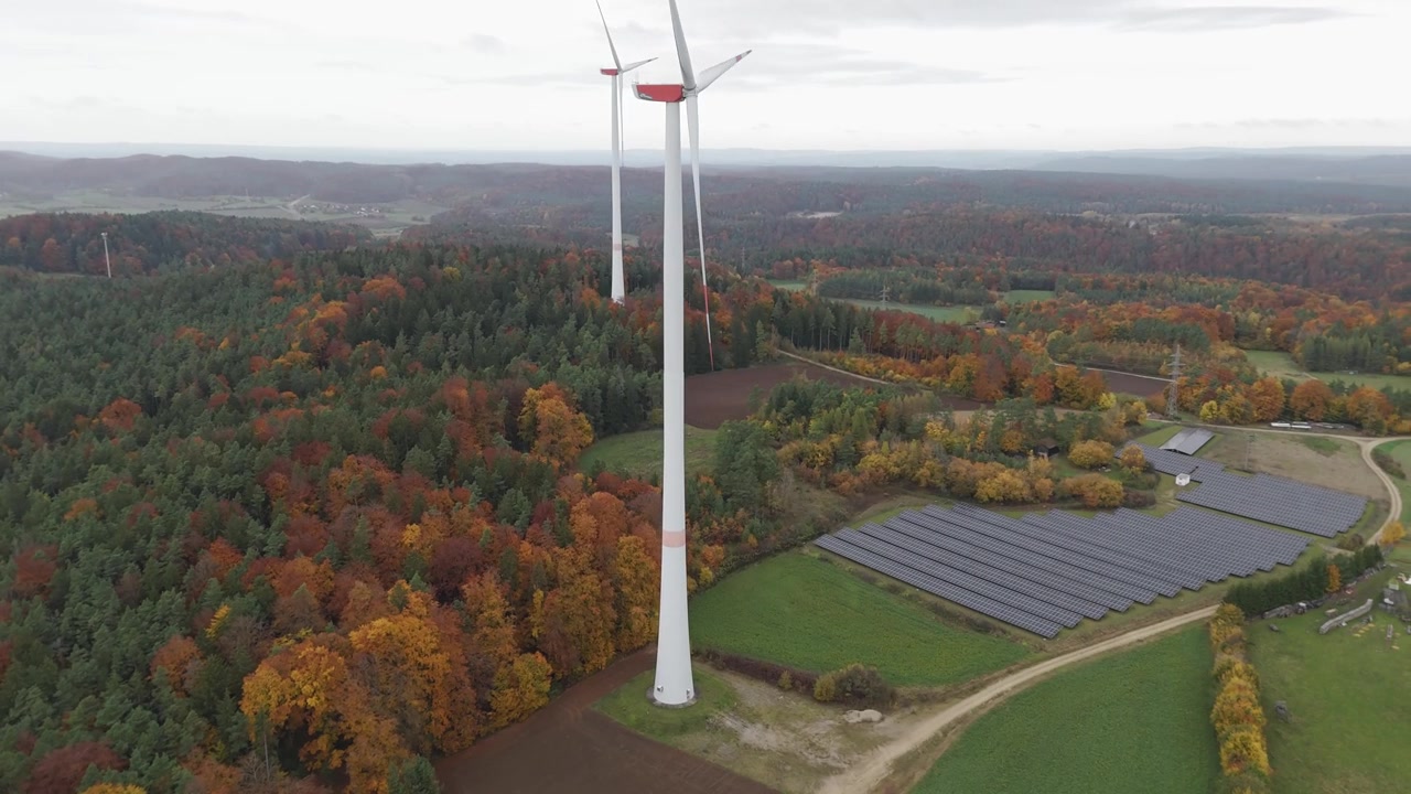Turbine eoliche si ergono sopra alberi autunnali colorati e pannelli solari in un suggestivo paesaggio rurale